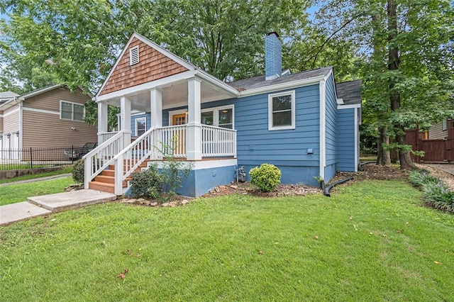 view of front of home featuring covered porch, a chimney, fence, and a front lawn