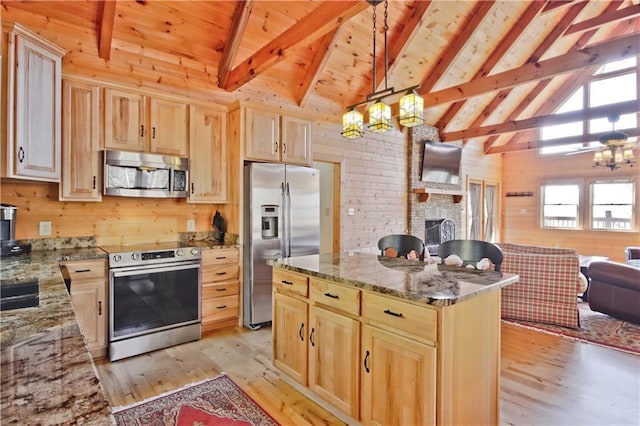 kitchen with open floor plan, light brown cabinetry, appliances with stainless steel finishes, and wooden walls