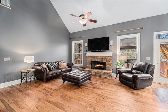 living room with ceiling fan, a stone fireplace, lofted ceiling, and light wood-type flooring