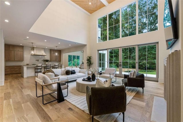 living room with french doors, a towering ceiling, a healthy amount of sunlight, and light wood-type flooring