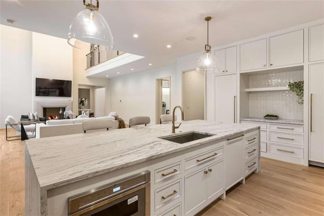 kitchen featuring light stone countertops, sink, an island with sink, white cabinets, and light wood-type flooring