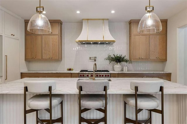 kitchen with a center island with sink, decorative backsplash, light brown cabinets, and premium range hood