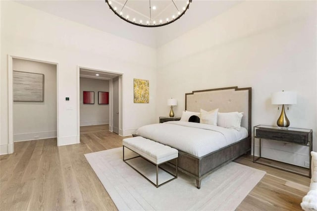 bedroom with light hardwood / wood-style flooring, a towering ceiling, and an inviting chandelier