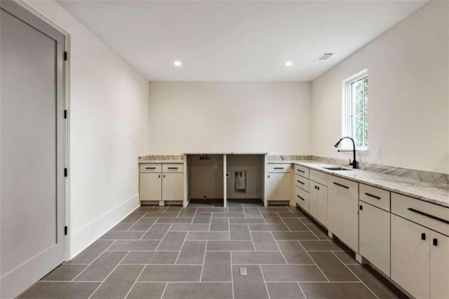 kitchen with cream cabinetry, dark tile patterned flooring, light stone countertops, and sink