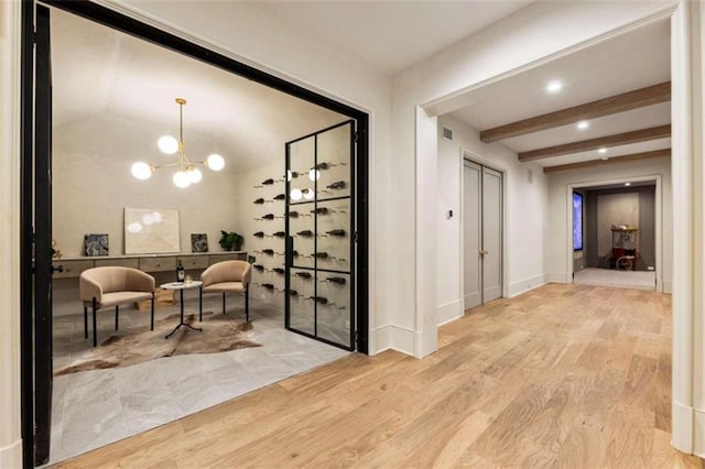 wine area featuring beam ceiling, light wood-type flooring, and an inviting chandelier