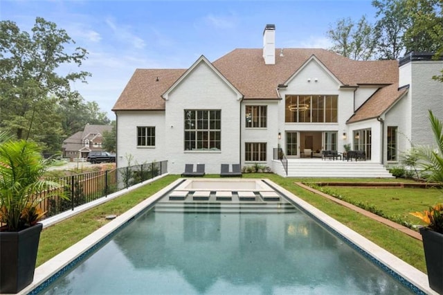 back of property with a fenced in pool and a lawn