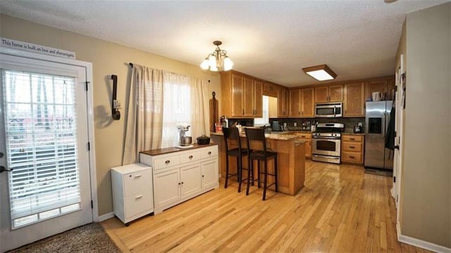 kitchen with light wood-style flooring, an inviting chandelier, appliances with stainless steel finishes, a healthy amount of sunlight, and a peninsula