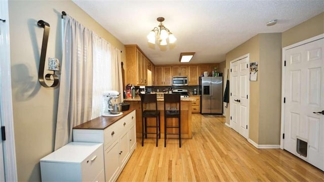 kitchen with stainless steel appliances, a peninsula, backsplash, light wood finished floors, and an inviting chandelier