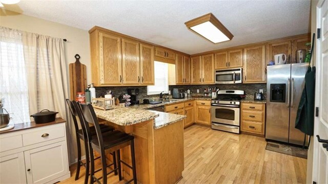 kitchen featuring appliances with stainless steel finishes, a peninsula, light wood-style floors, a chandelier, and a wealth of natural light