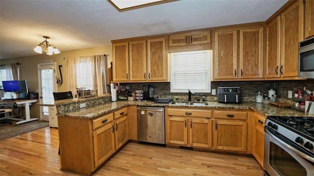 kitchen with appliances with stainless steel finishes, a sink, a peninsula, and light wood-style flooring