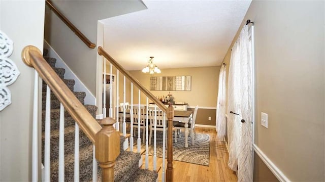 stairway featuring an inviting chandelier, baseboards, and wood finished floors