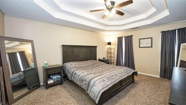 carpeted bedroom featuring ceiling fan, a tray ceiling, visible vents, and baseboards