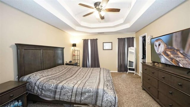 bedroom featuring light carpet, baseboards, a raised ceiling, and a ceiling fan