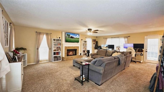 carpeted living area featuring a textured ceiling, a fireplace, and a ceiling fan