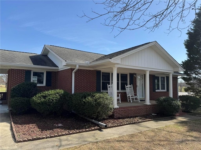 view of front facade with brick siding, roof with shingles, and a porch