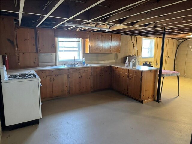 kitchen featuring concrete floors, a sink, white range with gas cooktop, light countertops, and plenty of natural light