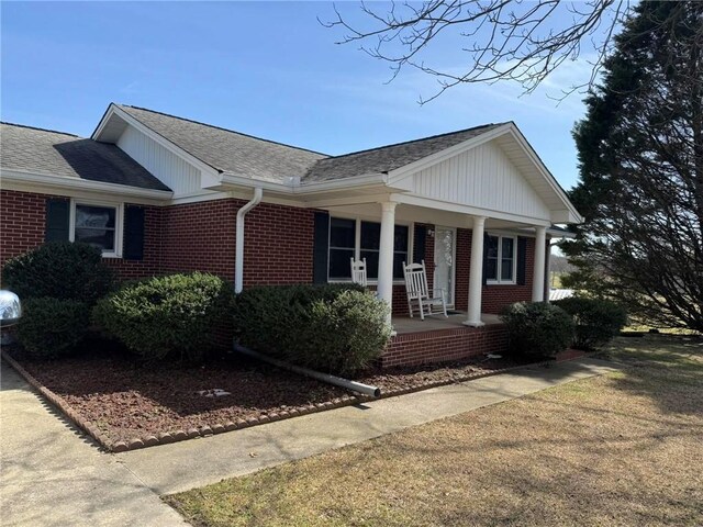 single story home with covered porch, roof with shingles, and brick siding