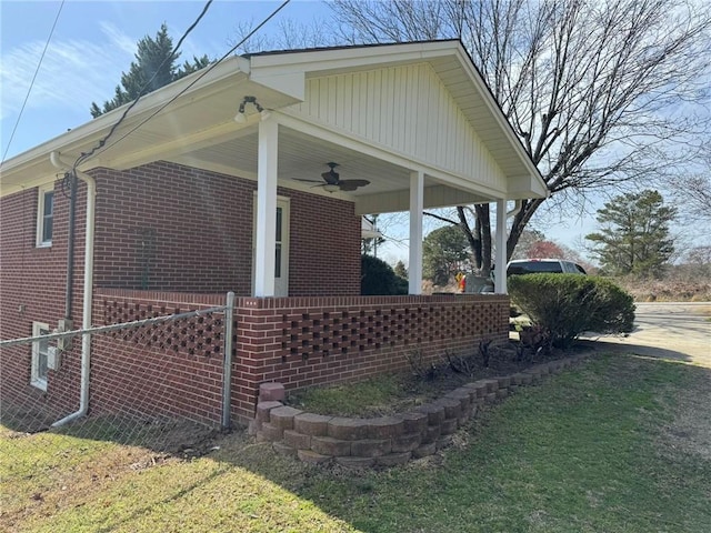 view of property exterior with brick siding, a lawn, and a ceiling fan