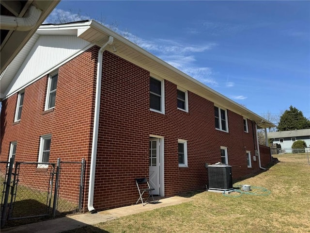 view of side of property featuring brick siding, central AC unit, and a gate