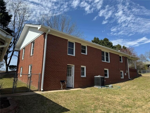 view of side of home with a yard, brick siding, central AC, and a gate