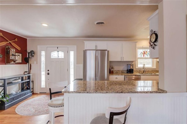 kitchen featuring a wealth of natural light, a breakfast bar area, white cabinets, light stone counters, and stainless steel appliances