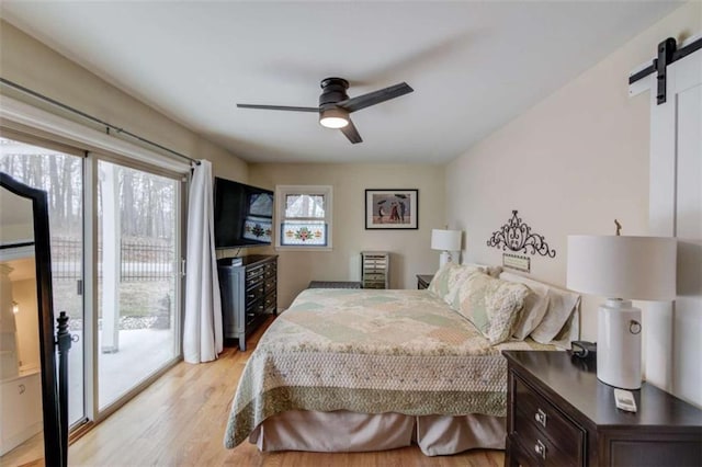 bedroom with a barn door, access to exterior, ceiling fan, and light hardwood / wood-style floors