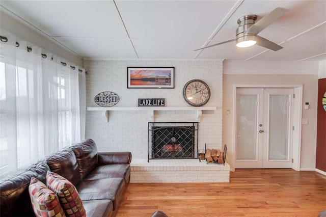 living room with french doors, ceiling fan, a brick fireplace, and light wood-type flooring