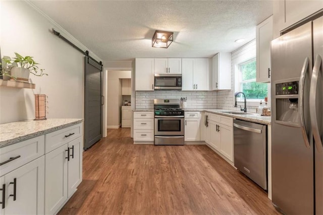 361 Princeton Way, Lawrenceville, GA 30044 - kitchen with appliances with stainless steel finishes, a barn door, white cabinetry, backsplash, and a textured ceiling