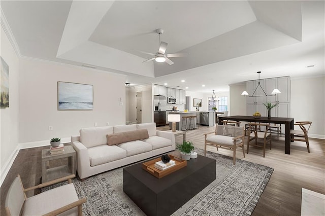 living room with a raised ceiling, ornamental molding, ceiling fan with notable chandelier, and hardwood / wood-style floors