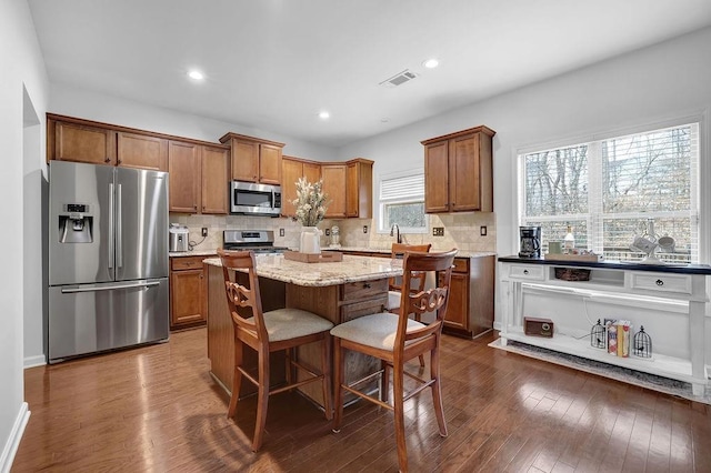 kitchen with a breakfast bar area, light stone counters, appliances with stainless steel finishes, dark hardwood / wood-style floors, and a kitchen island