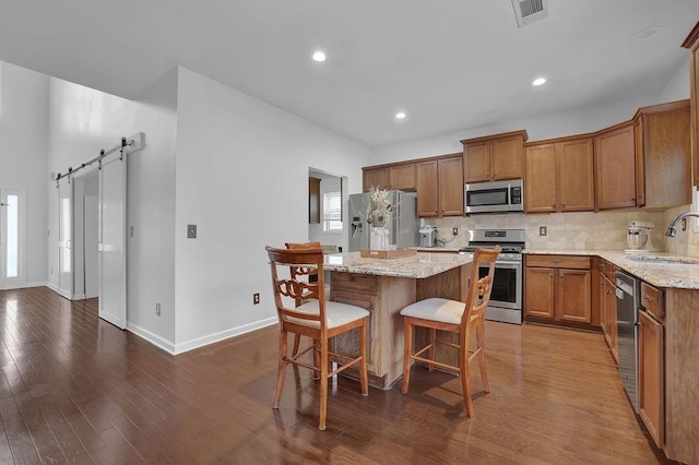 kitchen with a kitchen island, appliances with stainless steel finishes, sink, a barn door, and light stone countertops