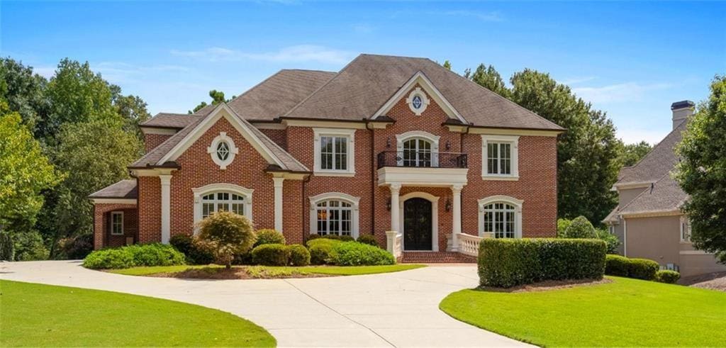 colonial home featuring a balcony, brick siding, curved driveway, and a front yard