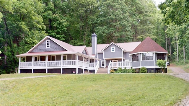 view of front facade with a chimney, a front yard, a wooded view, and a sunroom