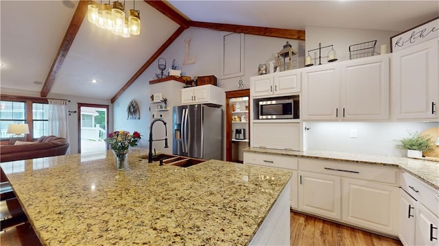 kitchen with light wood finished floors, appliances with stainless steel finishes, light stone counters, white cabinetry, and a sink