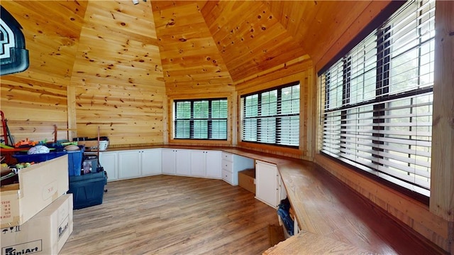 home office with light wood-type flooring, built in study area, vaulted ceiling, and wooden walls