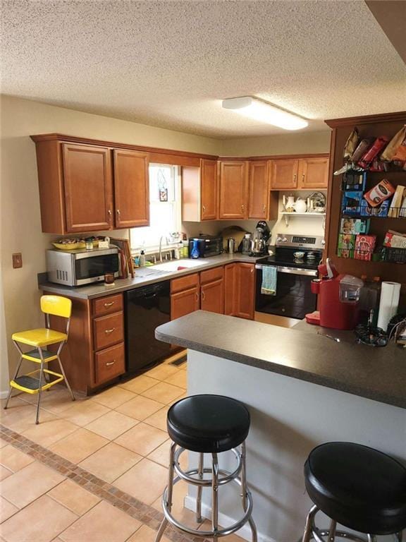 kitchen featuring light tile patterned floors, a sink, appliances with stainless steel finishes, a textured ceiling, and a kitchen breakfast bar