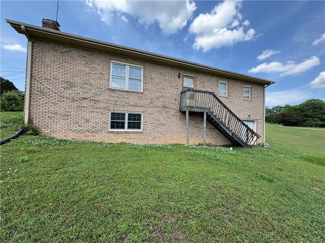 rear view of house featuring a lawn, brick siding, stairs, and a chimney