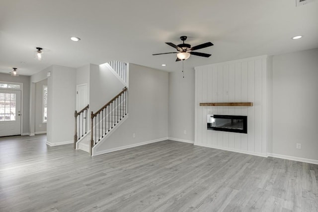 unfurnished living room featuring a fireplace, recessed lighting, stairway, wood finished floors, and baseboards