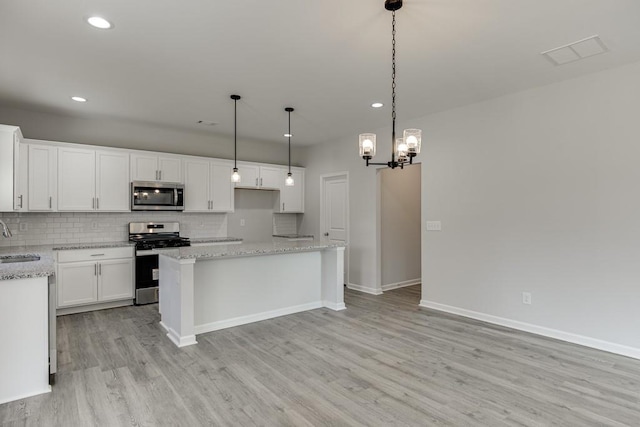 kitchen featuring stainless steel appliances, backsplash, white cabinets, a sink, and light wood-type flooring