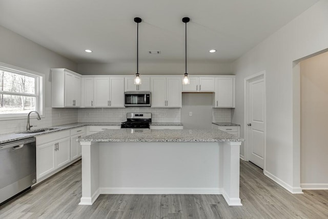 kitchen with appliances with stainless steel finishes, a center island, white cabinets, and a sink