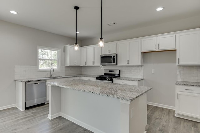 kitchen featuring visible vents, white cabinets, a kitchen island, stainless steel appliances, and a sink