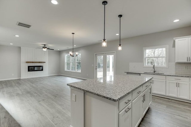 kitchen featuring visible vents, decorative backsplash, a large fireplace, a kitchen island, and a sink