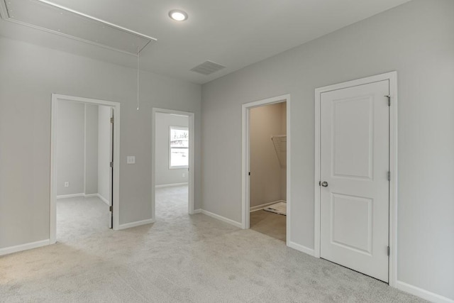 unfurnished bedroom featuring carpet floors, visible vents, baseboards, a walk in closet, and attic access