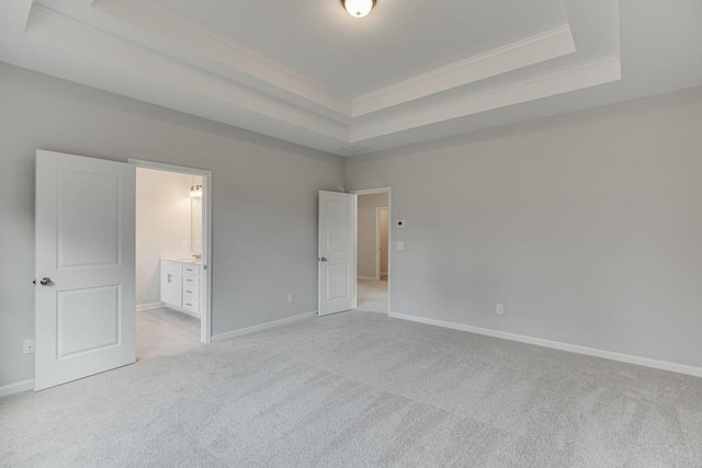 unfurnished bedroom with baseboards, a raised ceiling, light colored carpet, ensuite bath, and crown molding