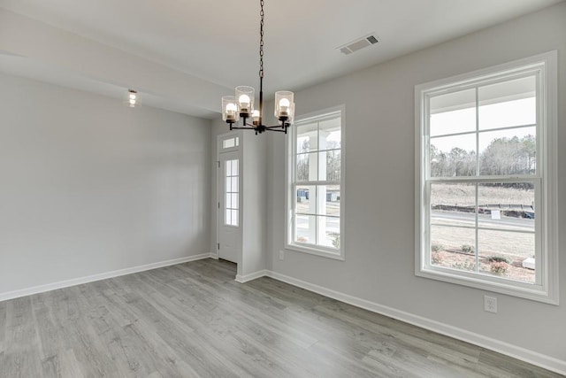 empty room featuring visible vents, a notable chandelier, baseboards, and wood finished floors