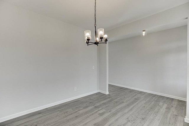 spare room featuring a chandelier, baseboards, and wood finished floors