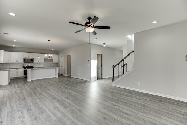 unfurnished living room with light wood-style floors, recessed lighting, stairway, and ceiling fan with notable chandelier