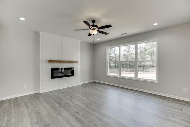 unfurnished living room featuring a large fireplace, baseboards, visible vents, wood finished floors, and recessed lighting