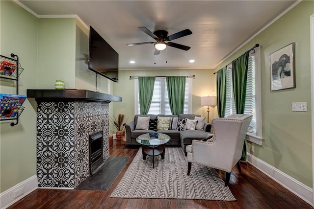 living room with crown molding, ceiling fan, dark wood-type flooring, and a tiled fireplace