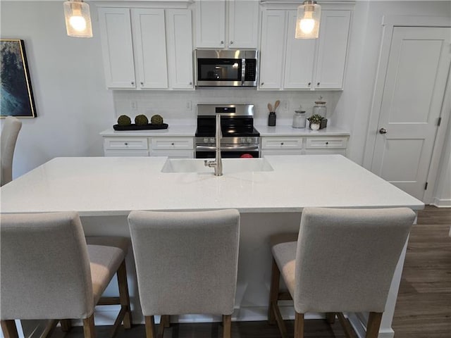 kitchen featuring pendant lighting, appliances with stainless steel finishes, a kitchen island with sink, a kitchen breakfast bar, and white cabinets